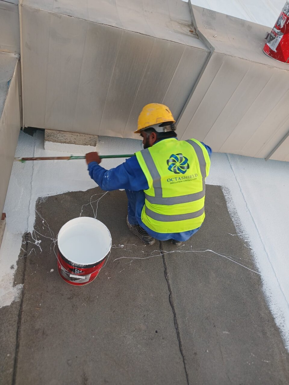 Worker applying silicone roof coating around AC ducts