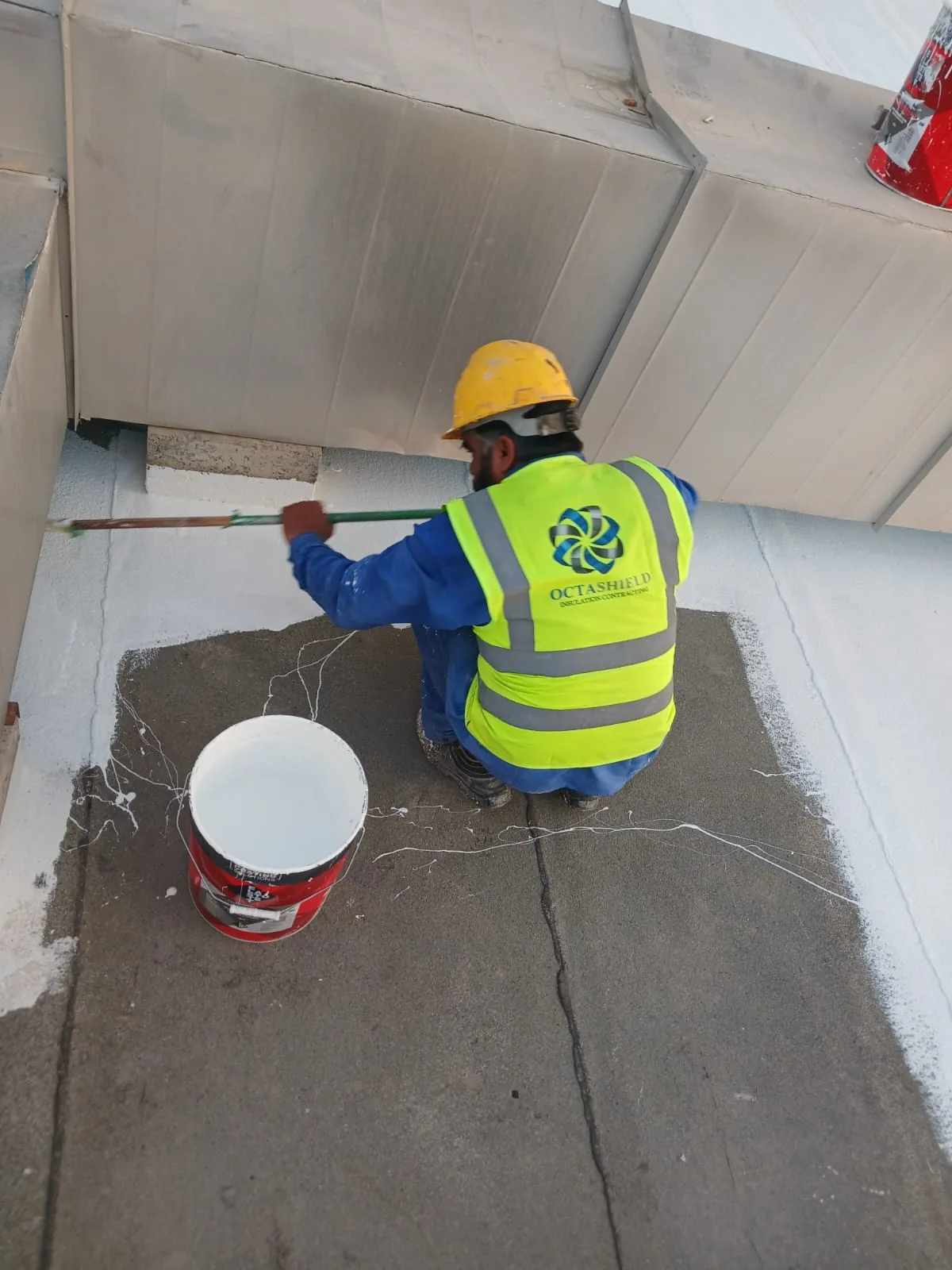 Worker applying silicone roof coating around AC ducts